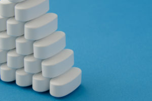 stacked hormone pellets white tablets pills on blue background with copy space
