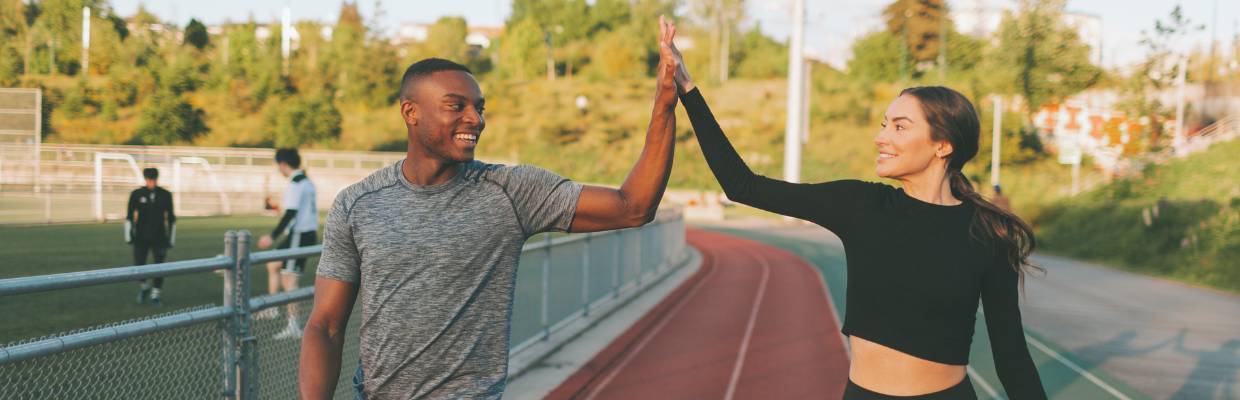 A man and a woman on a running track giving each other high 5's